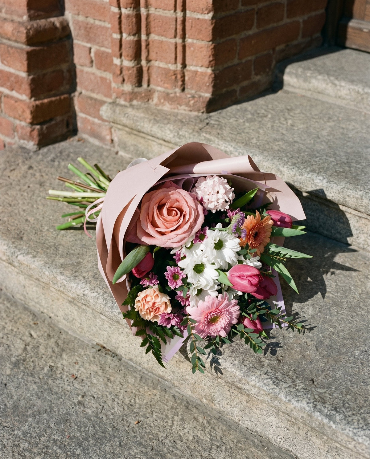 Antologia, bouquet di rose, gerbere e tulipani di Emozioni appoggiato su un gradino di pietra a Torino