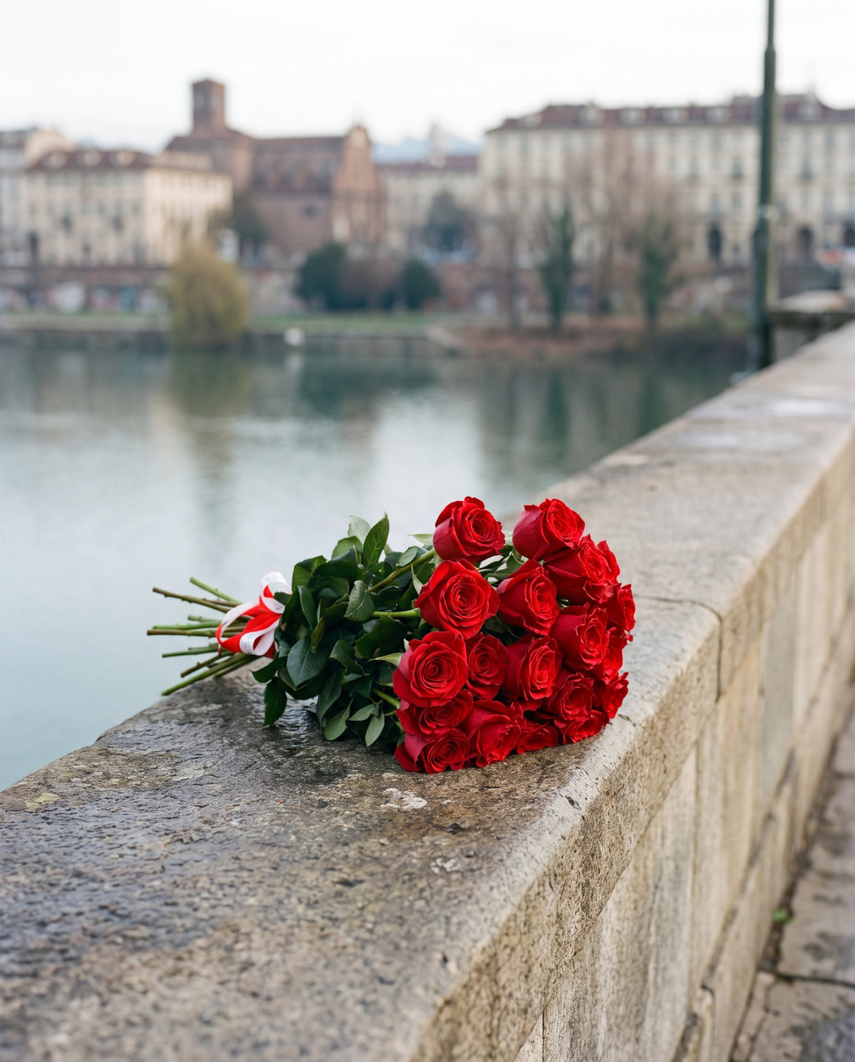Mazzo di rose rosse a gambo lungo di Emozioni appoggiato sul parapetto del Po a Torino