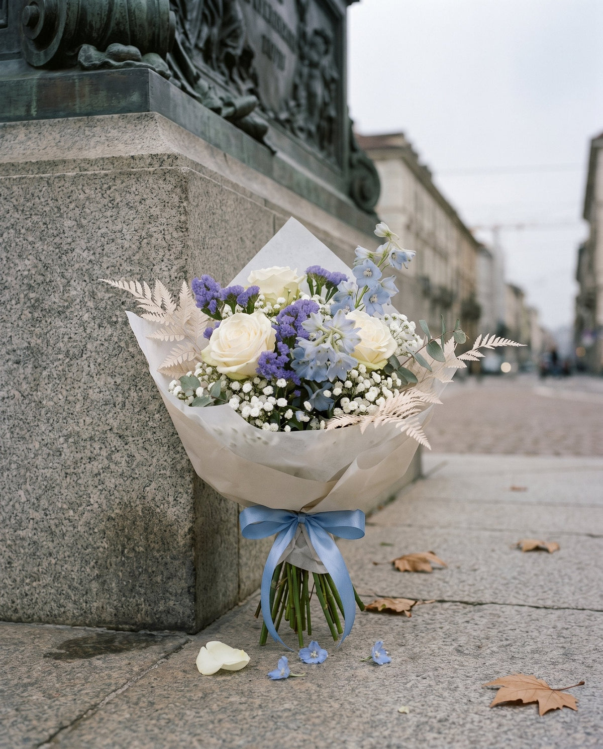 Bouquet di laurea con rose bianche e fiori blu appoggiato ai piedi di una statua a Torino
